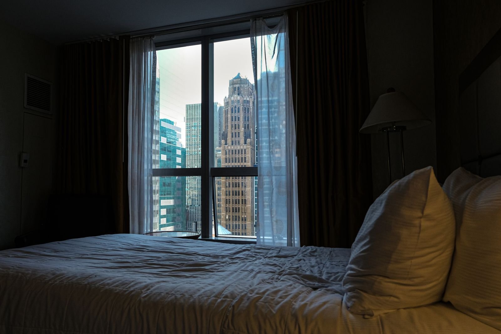 Bedroom with a large window looking out over a city at dusk