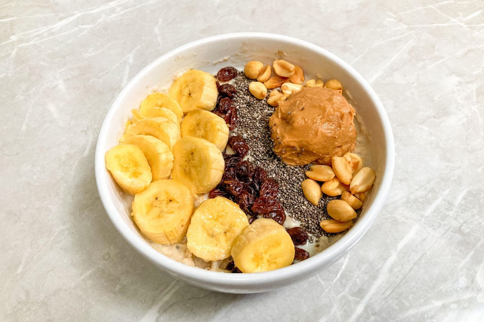 Breakfast bowl with sliced banana, chia seeds, peanuts and peanut butter