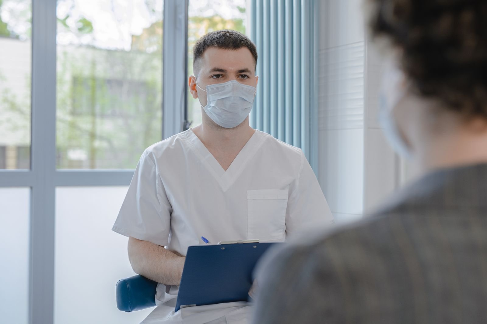 Clinician in scrubs taking notes while talking with a male patient