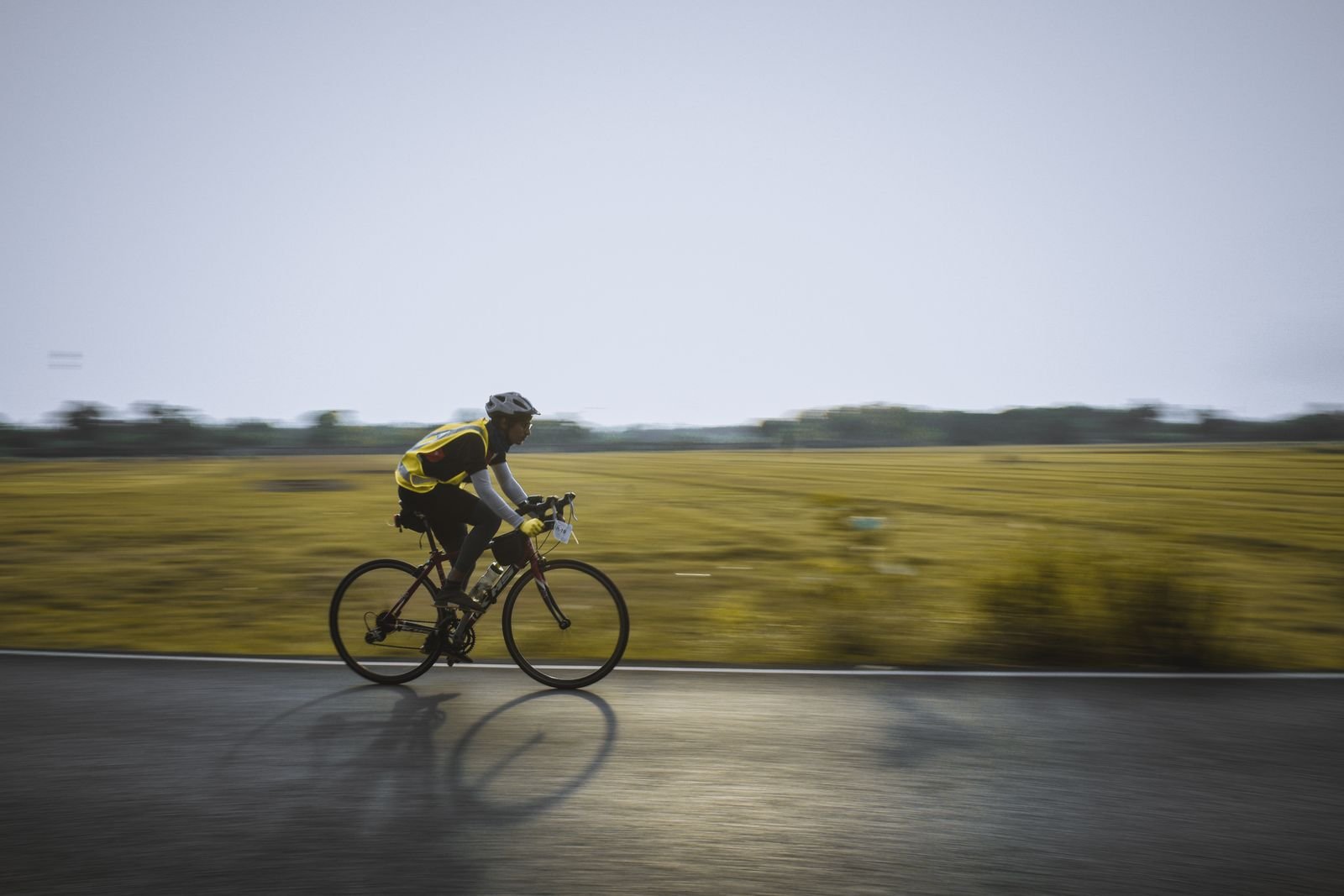 Cyclist in a helmet riding along a road beside green fields