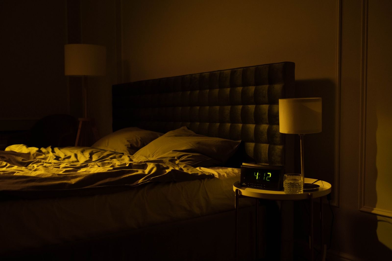 Dim bedroom with an unmade bed and a digital clock showing 4:12