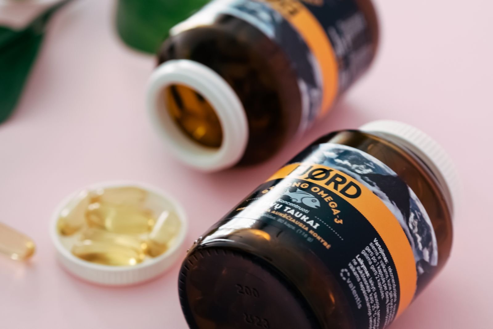 Fish oil capsules in clear bottles on a pink background