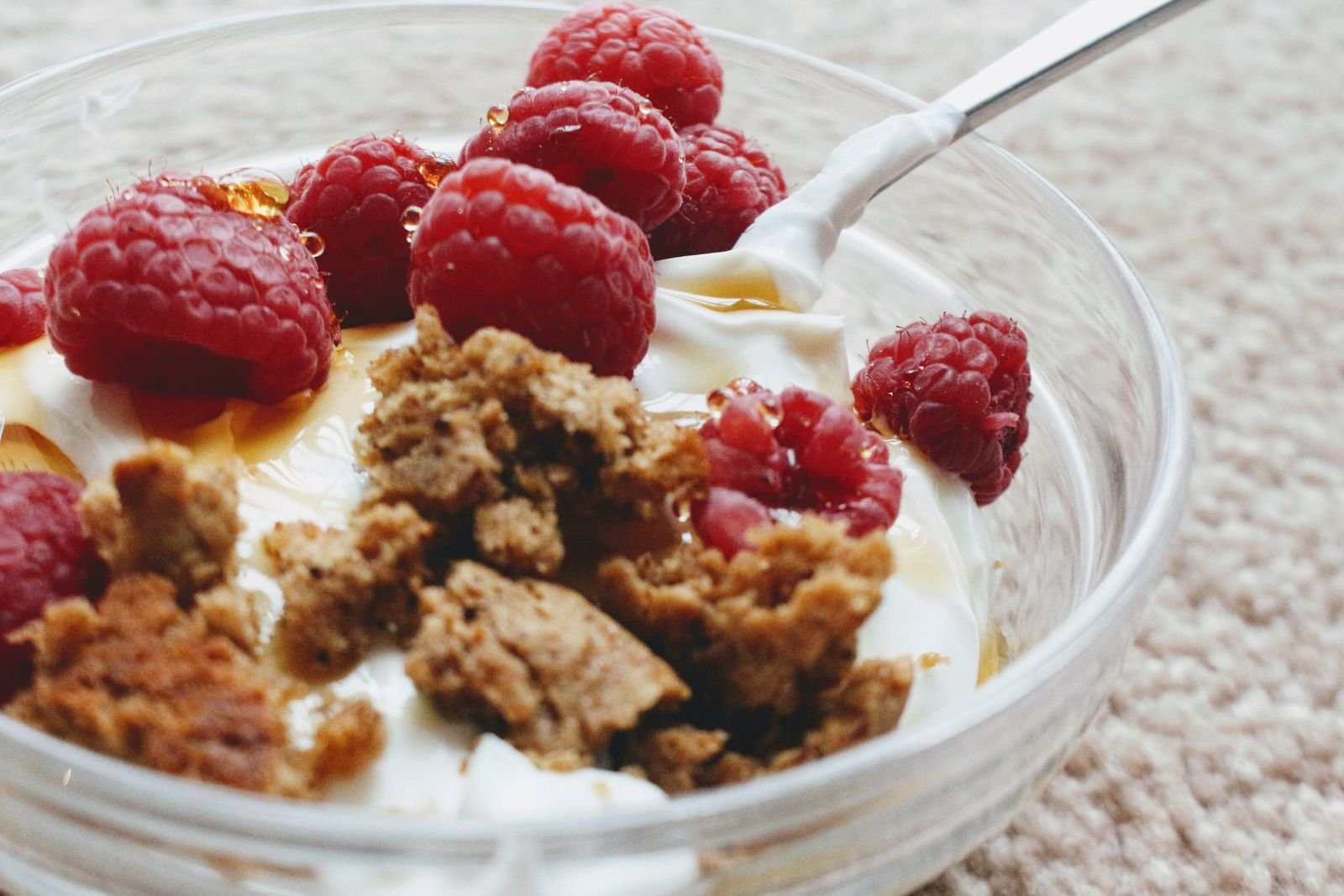 Glass bowl of natural yogurt topped with fresh raspberries