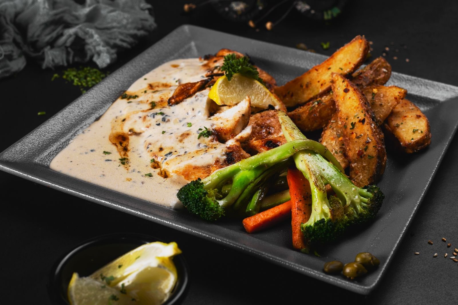 Grilled chicken breast with broccoli and roast potatoes on a dark plate