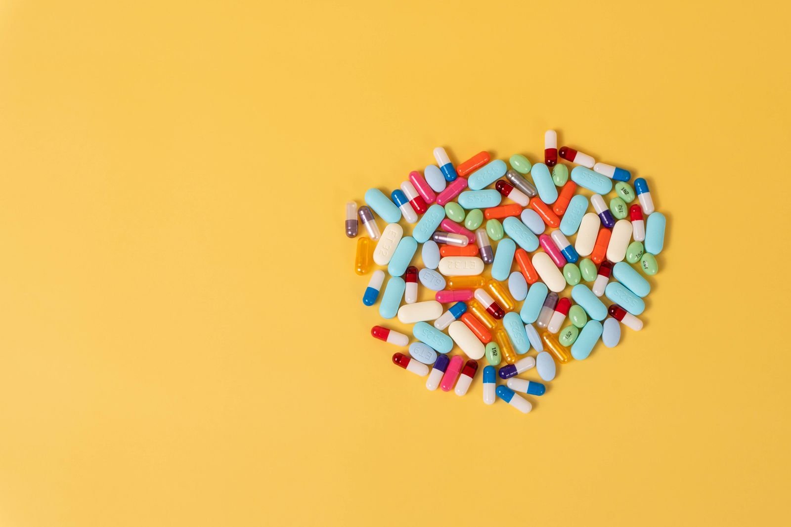 Heart-shaped pile of assorted pills on a yellow background
