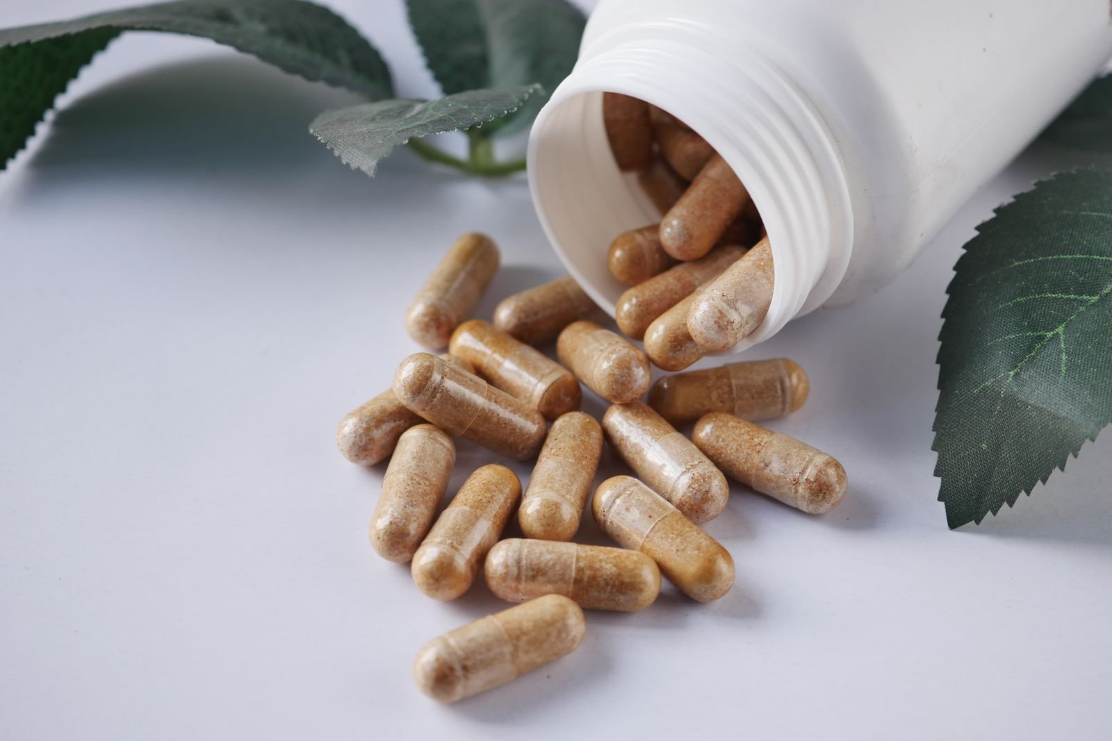 Herbal capsules spilling from a bottle beside green leaves