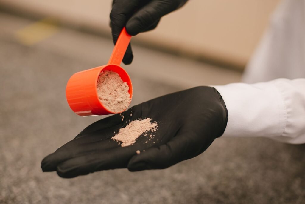 Gloved hand pouring pre-workout powder from a scoop