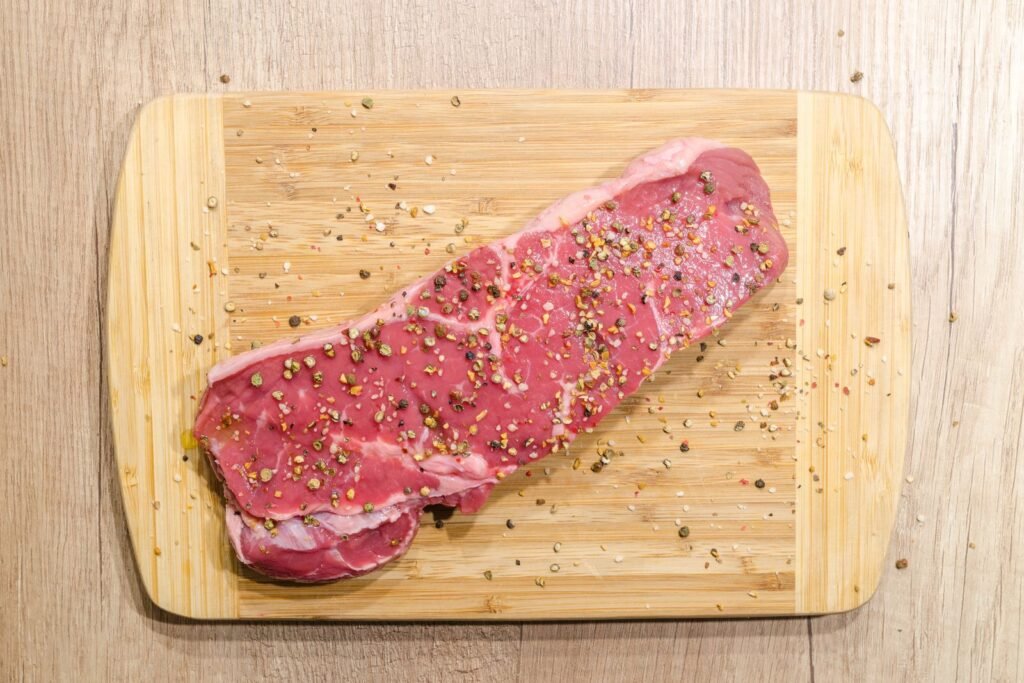 Raw beef steak seasoned with spices on a wooden board