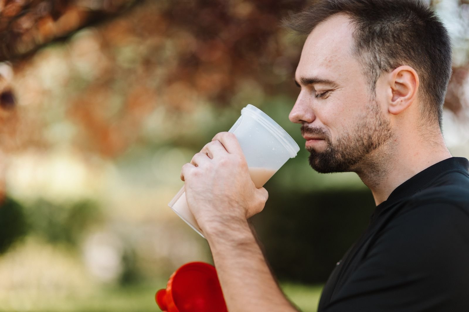 Man drinking a protein shake from a shaker bottle outdoors