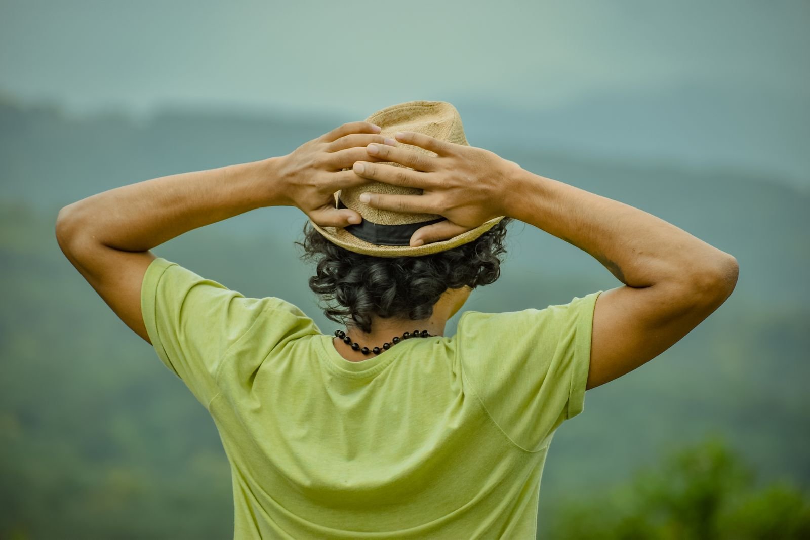 Man in a hat with his hands on his head, looking out at the mountains