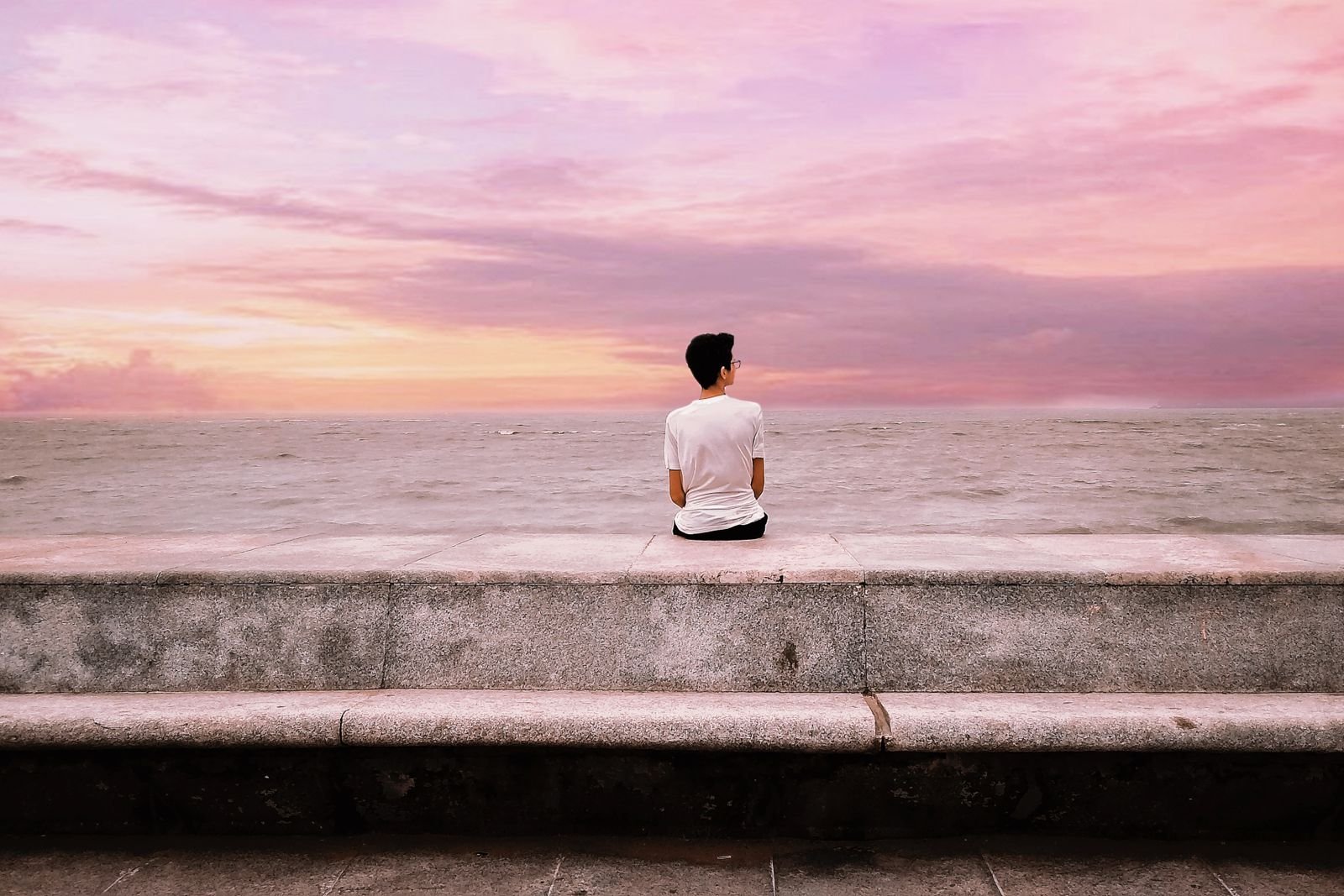 Man sitting alone on a seafront wall at sunset