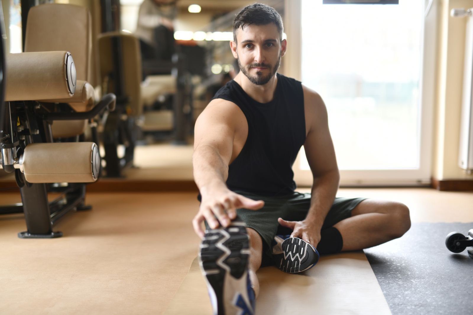 Man sitting on a gym floor stretching his hamstrings