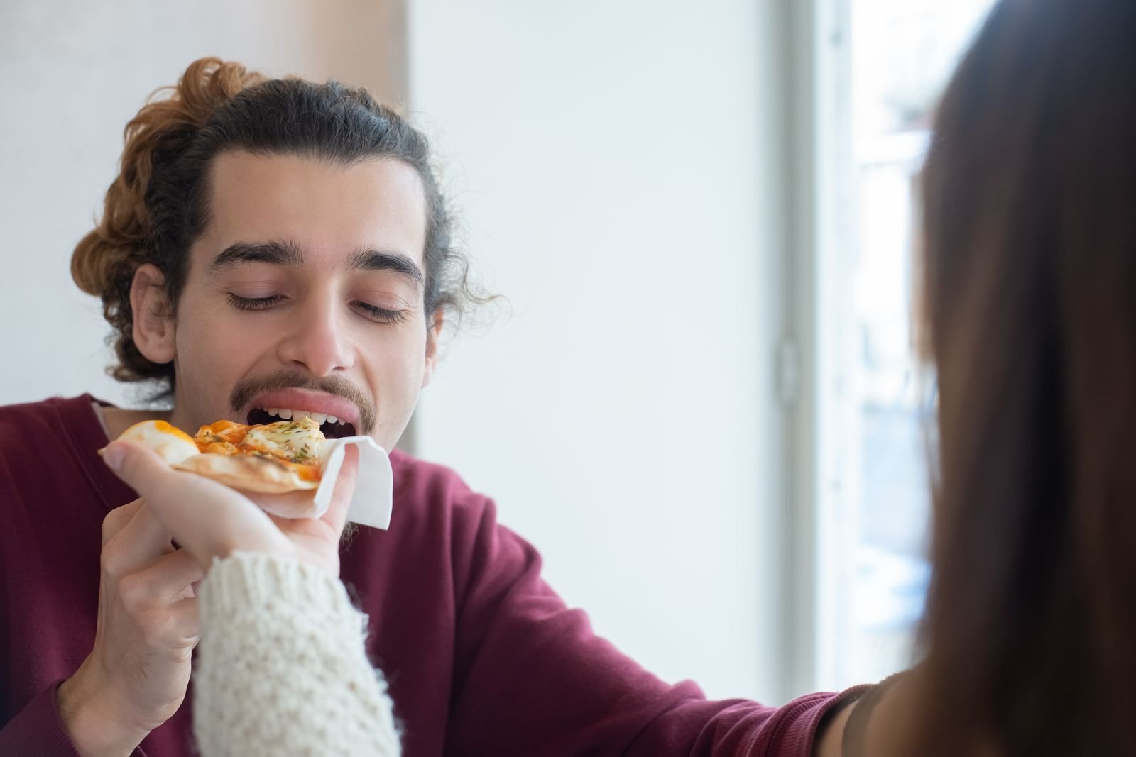 Man taking a bite of pizza offered by a friend