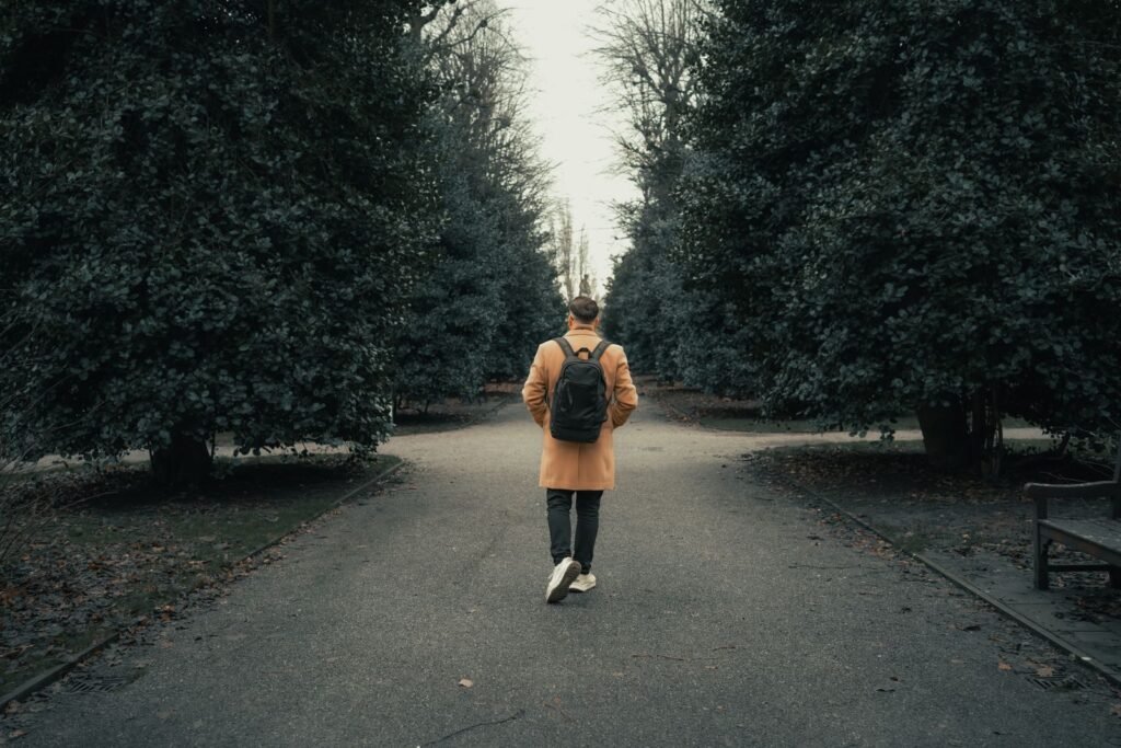 Man with a backpack walking down a tree-lined road