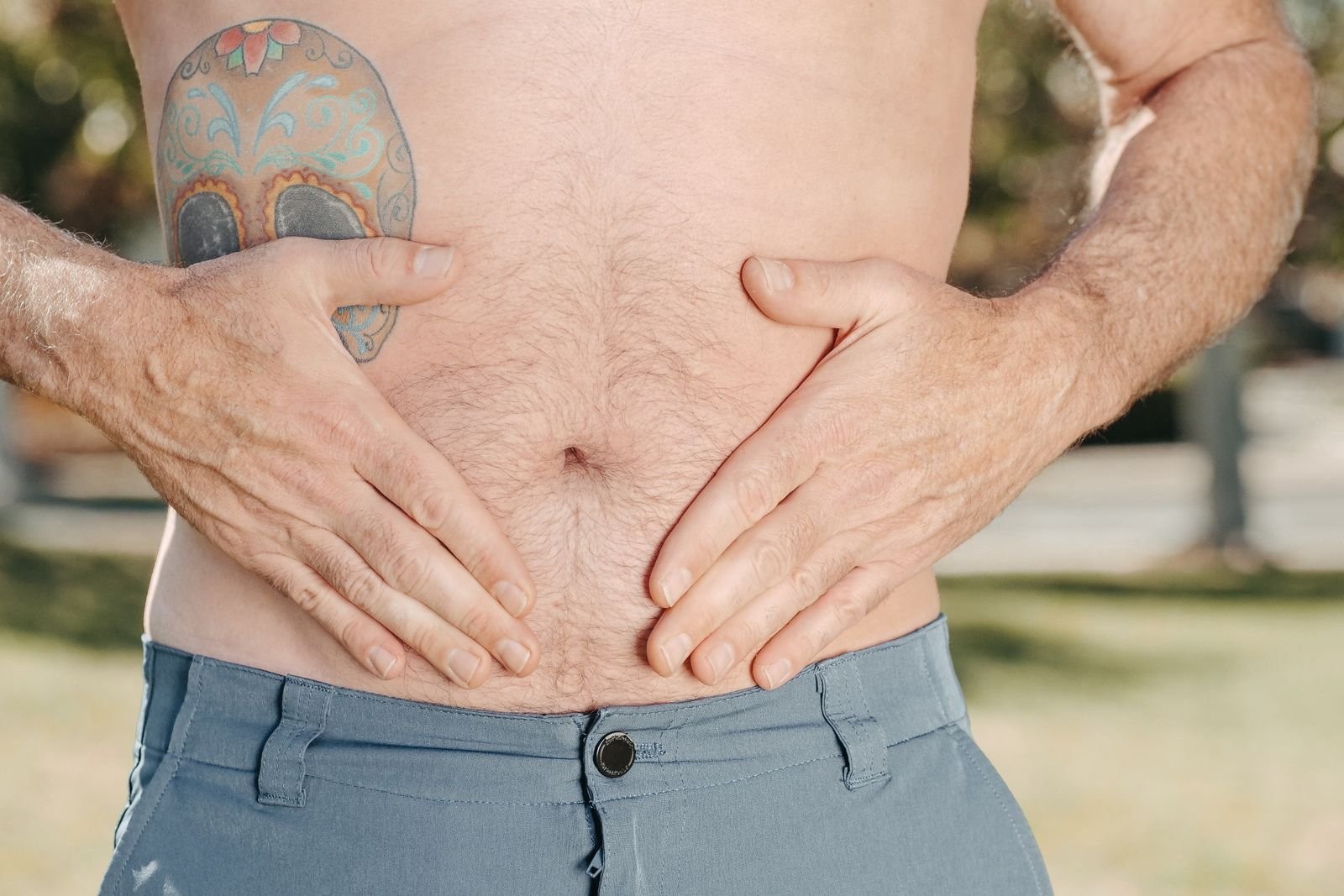 Man with a tattooed torso holding his stomach outdoors