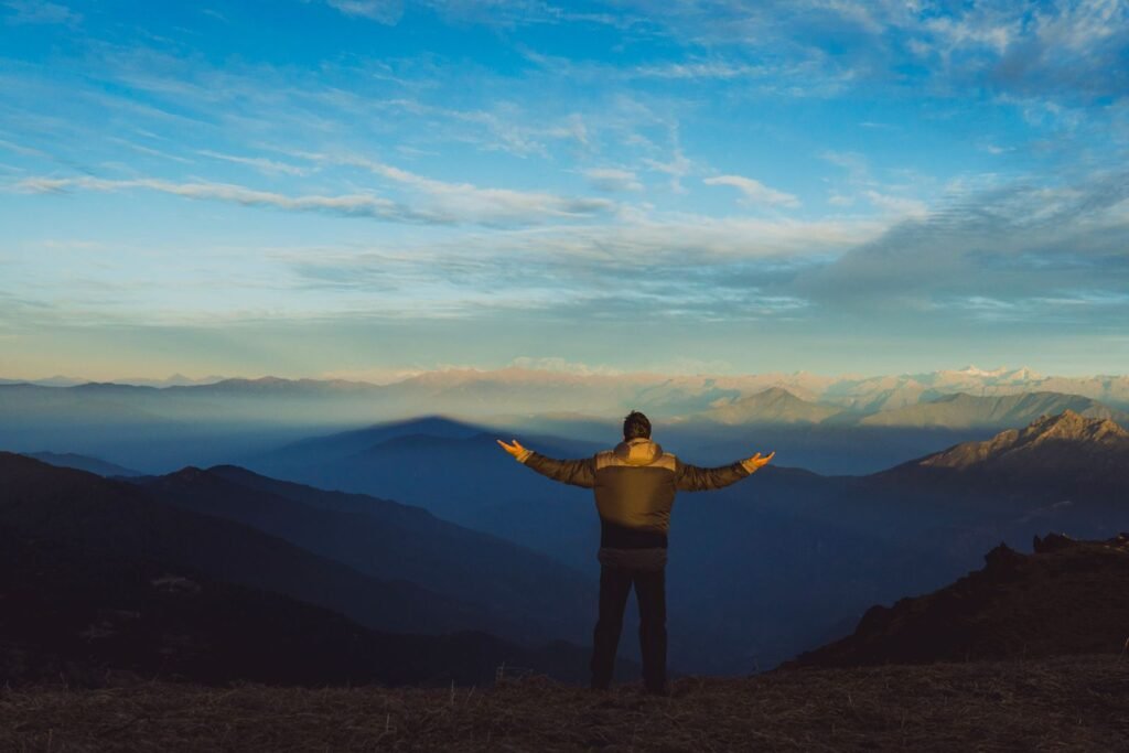 Man with arms outstretched above a mountain valley at sunrise