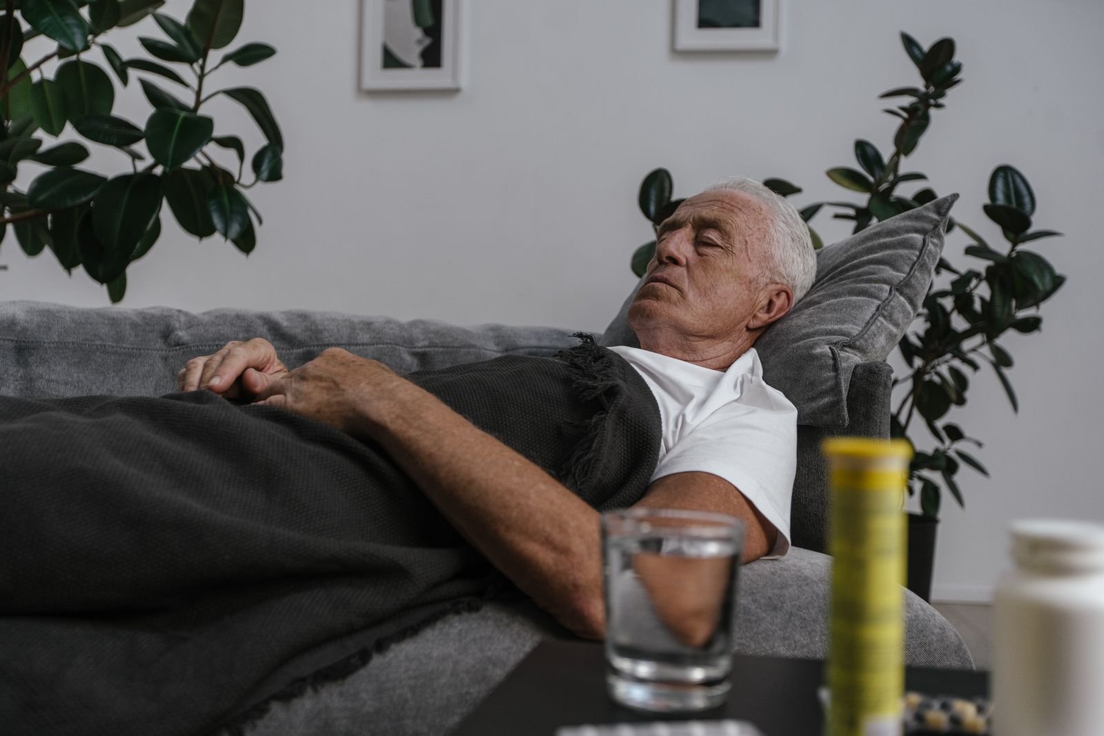 Older man asleep on a sofa under a blanket, a glass of water beside him