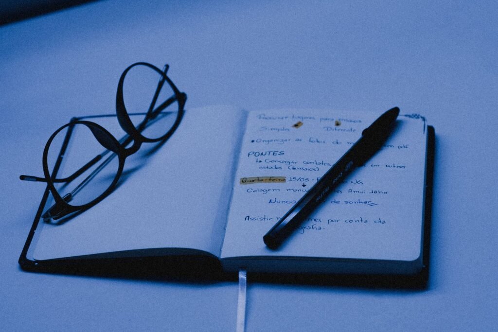 Open notebook with a pen and glasses on a desk