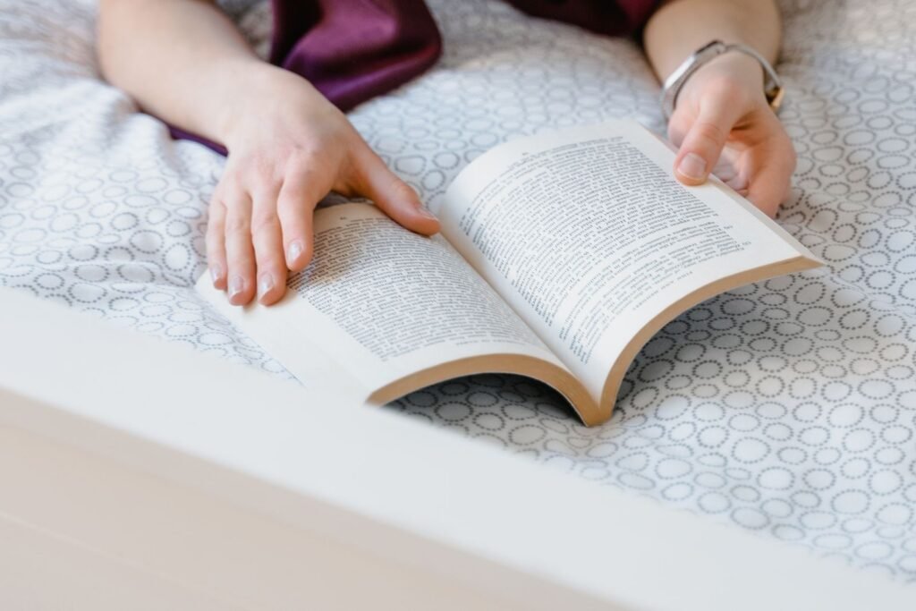 Person lying on a bed reading an open book