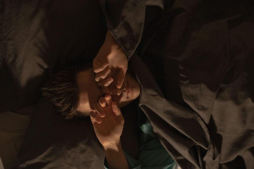 Man lying in bed covering his eyes with a pillow