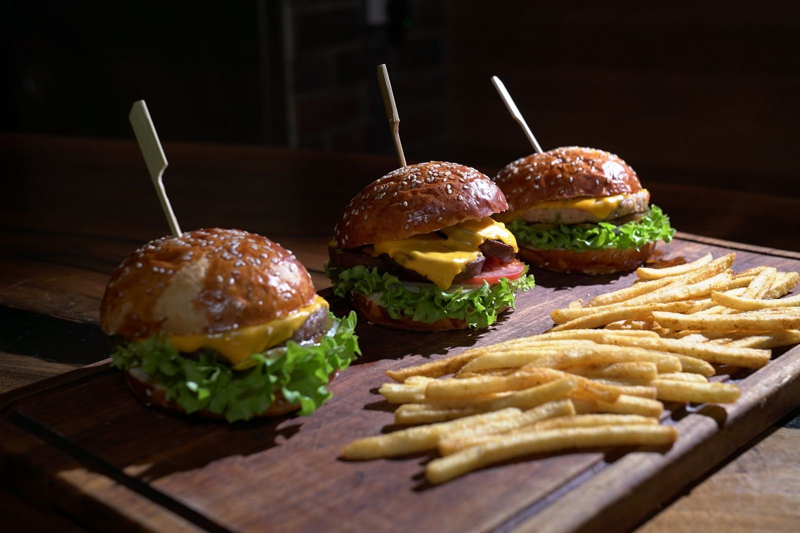Three cheeseburgers and fries on a wooden platter