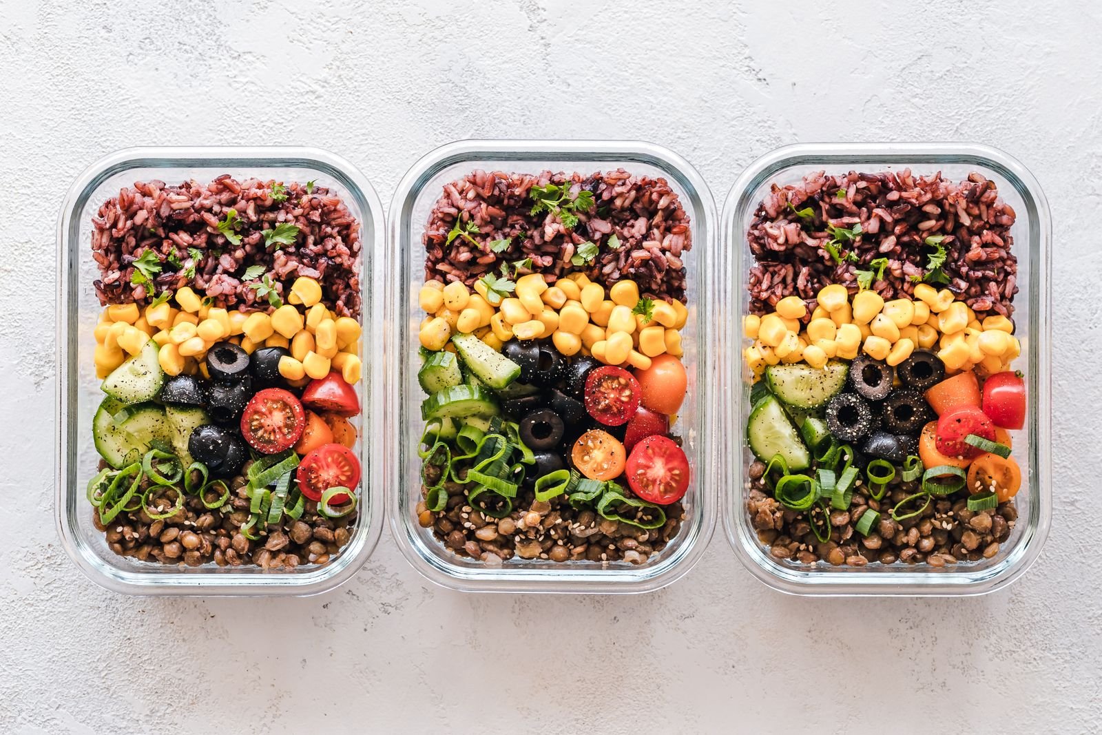 Three meal prep containers filled with grains, vegetables and beans