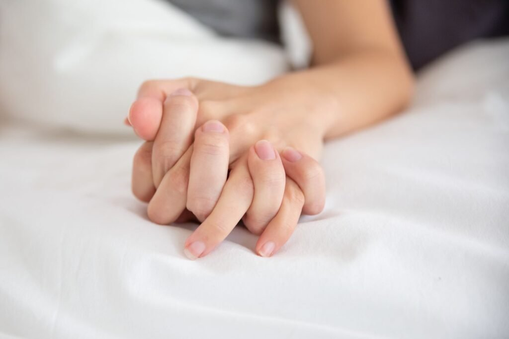 Two hands clasped together on white sheets