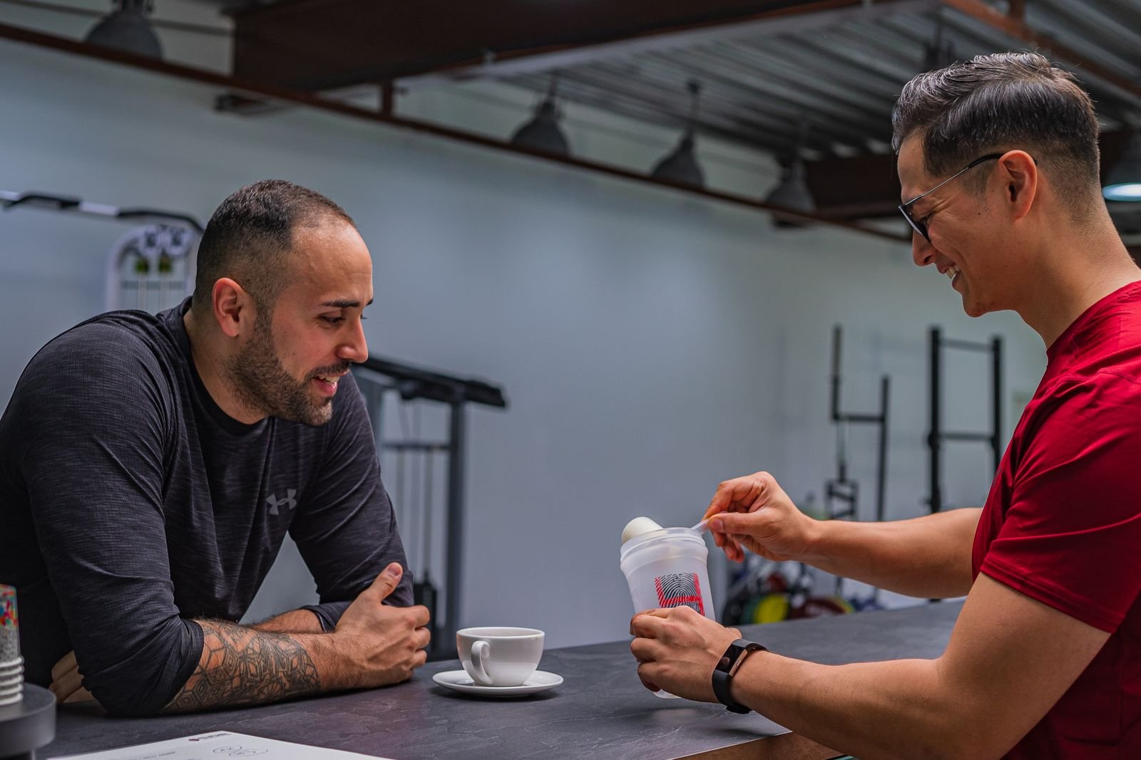 Two men at a gym counter mixing a protein shake