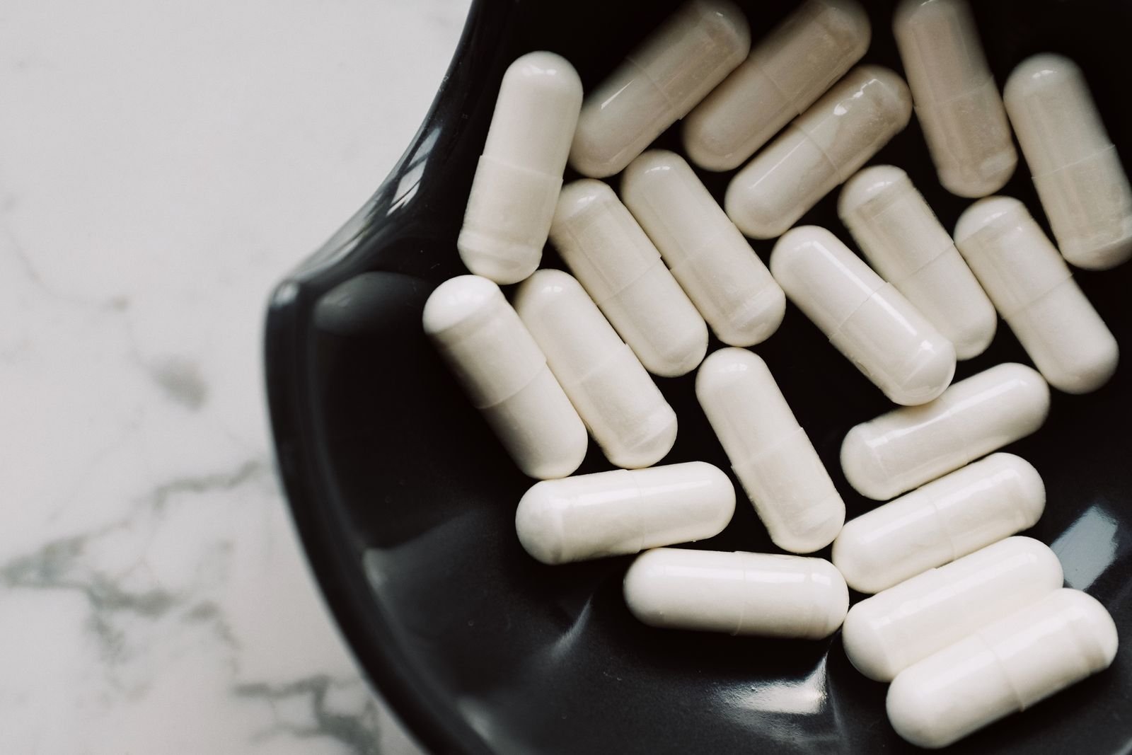 White capsules in a black bowl on a marble surface