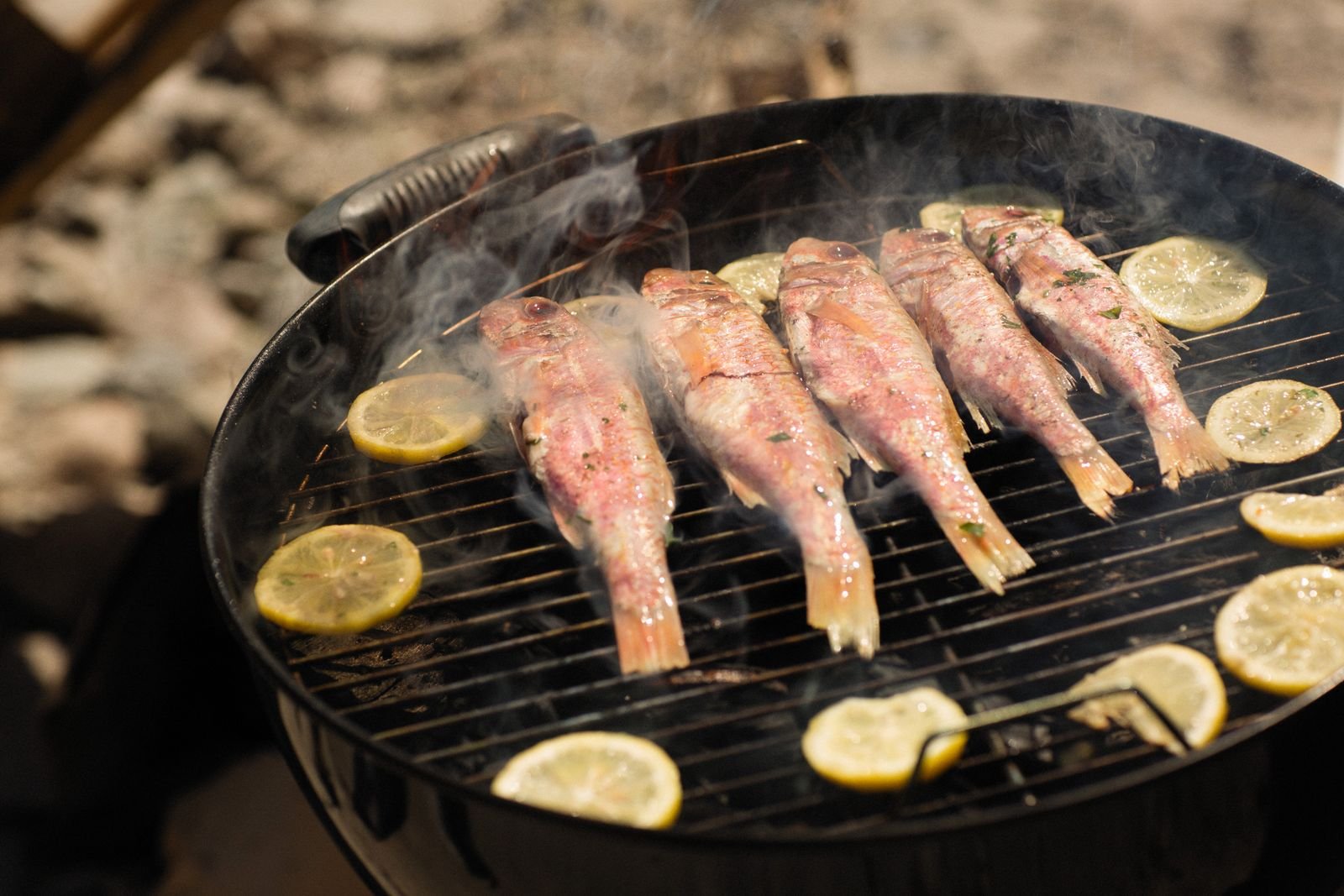 Whole fish grilling with lemon slices on a barbecue