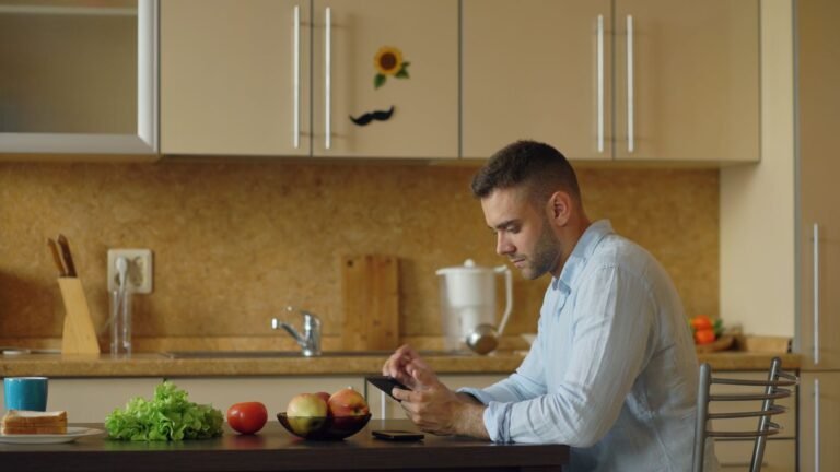 Man checking his phone in a kitchen with fresh vegetables, wondering why he is not losing weight
