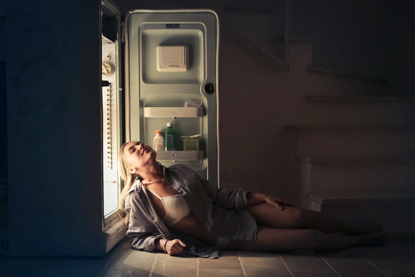 Woman sitting by an open fridge in a dark kitchen