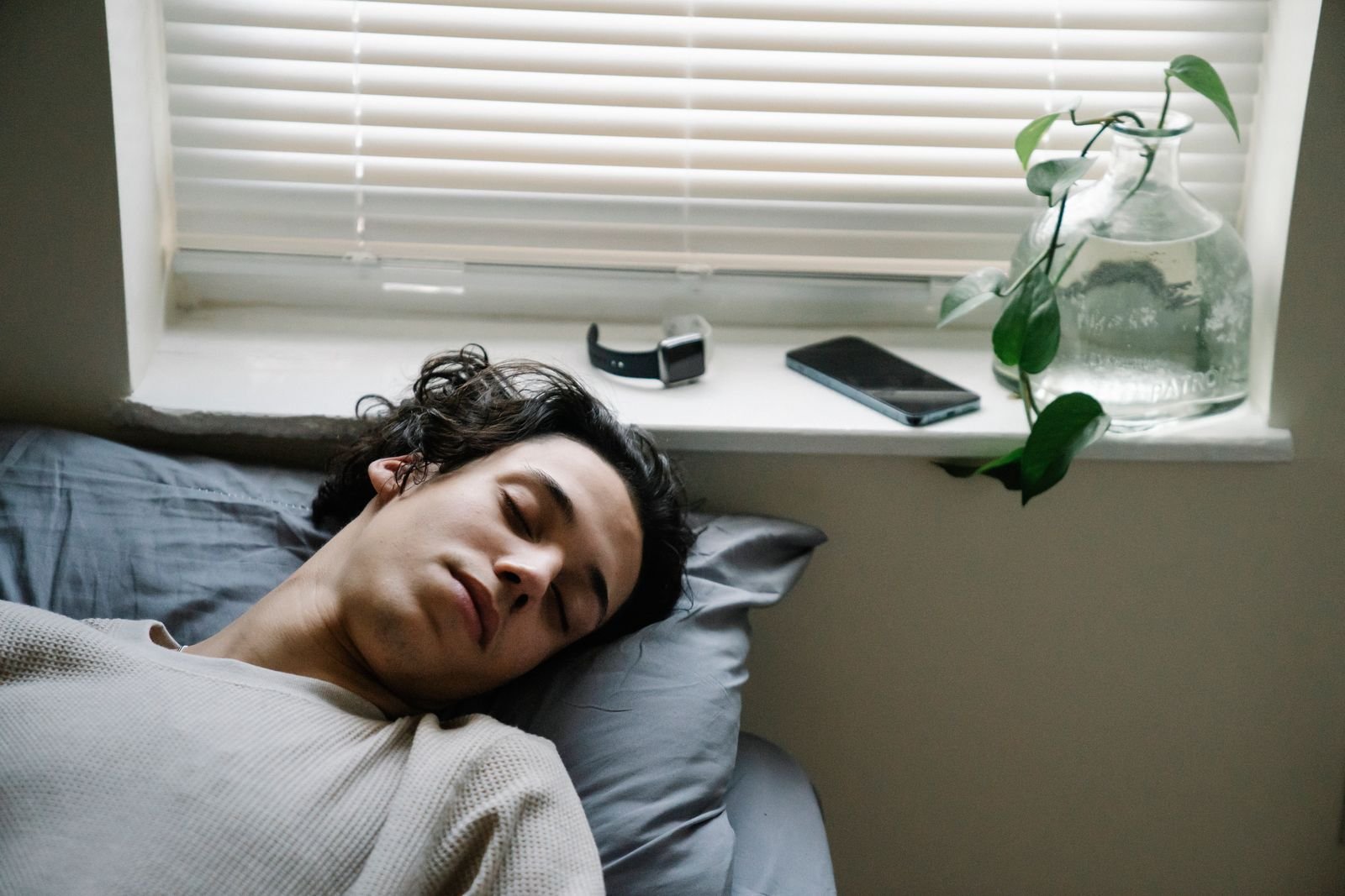 Young man asleep in bed with his phone and watch on the windowsill