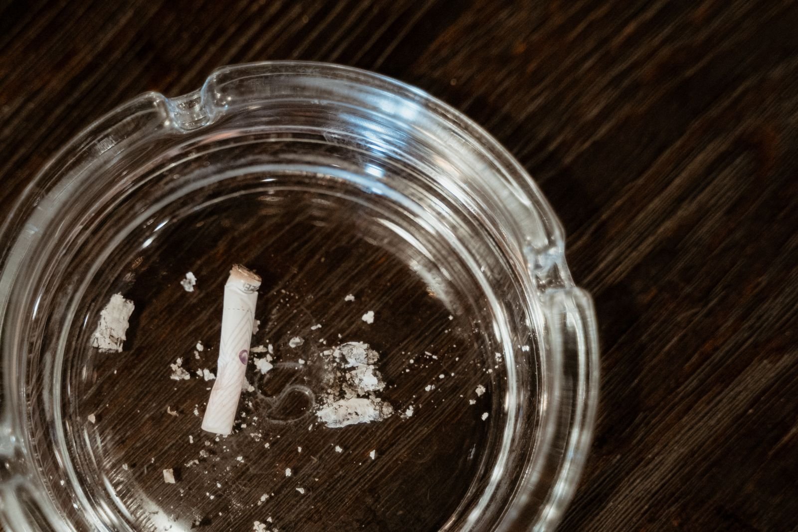 Cigarette butt left from smoking in a glass ashtray on a dark wooden table