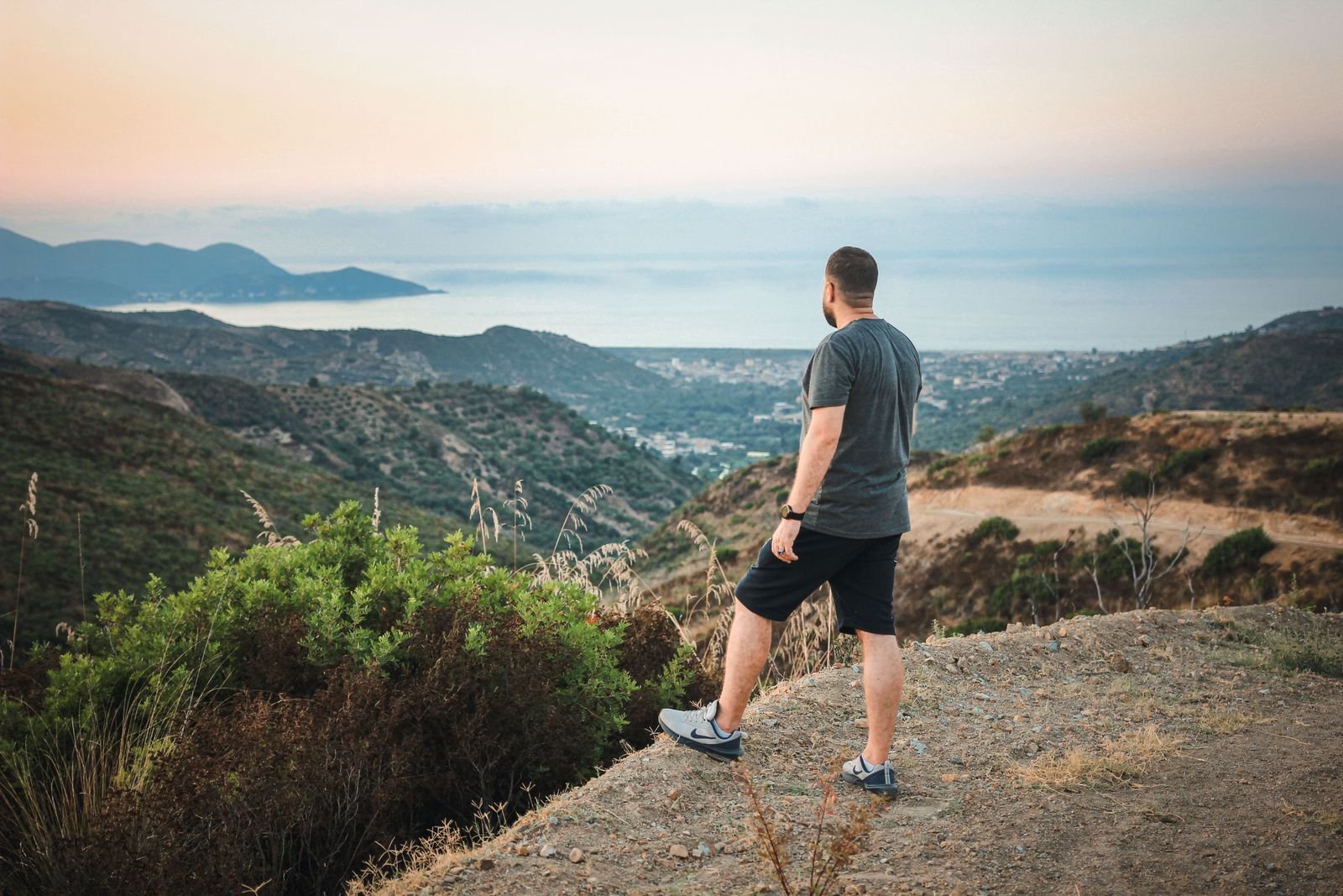 Man looking out over hills and the sea at sunset, seen from behind