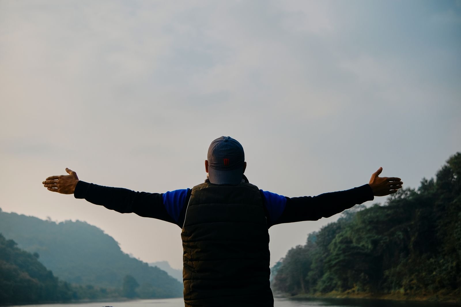 Man stretching his arms wide outdoors, seen from behind