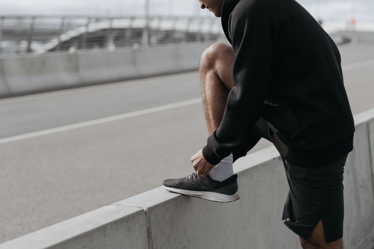 Man tying his running shoe on a concrete barrier before a run