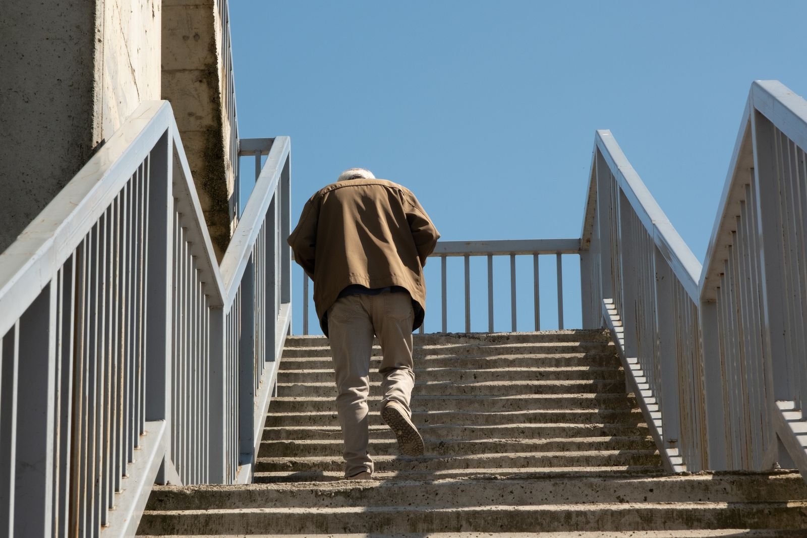 Older man climbing outdoor concrete steps, seen from behind