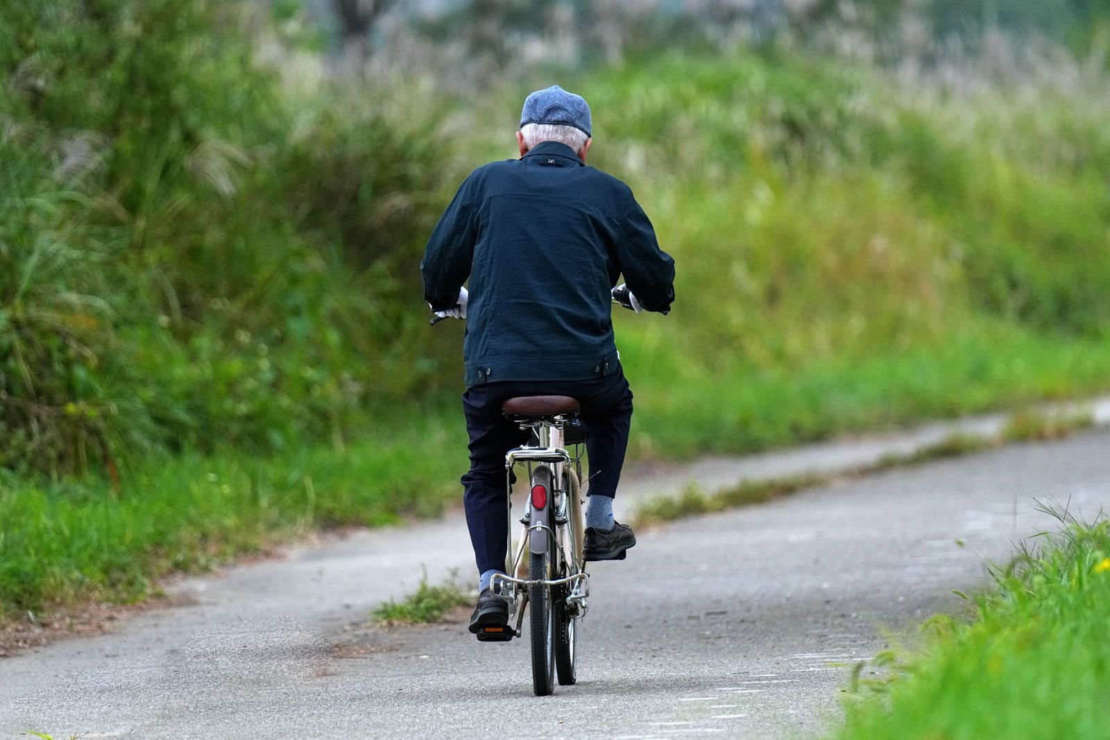 Older man cycling on a country road, seen from behind