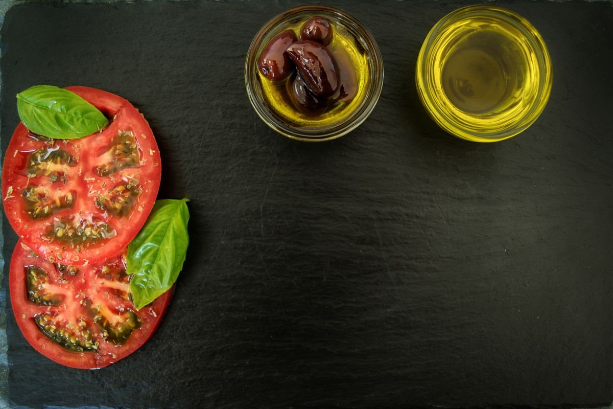 Sliced tomatoes, basil, olives and olive oil on a dark slate
