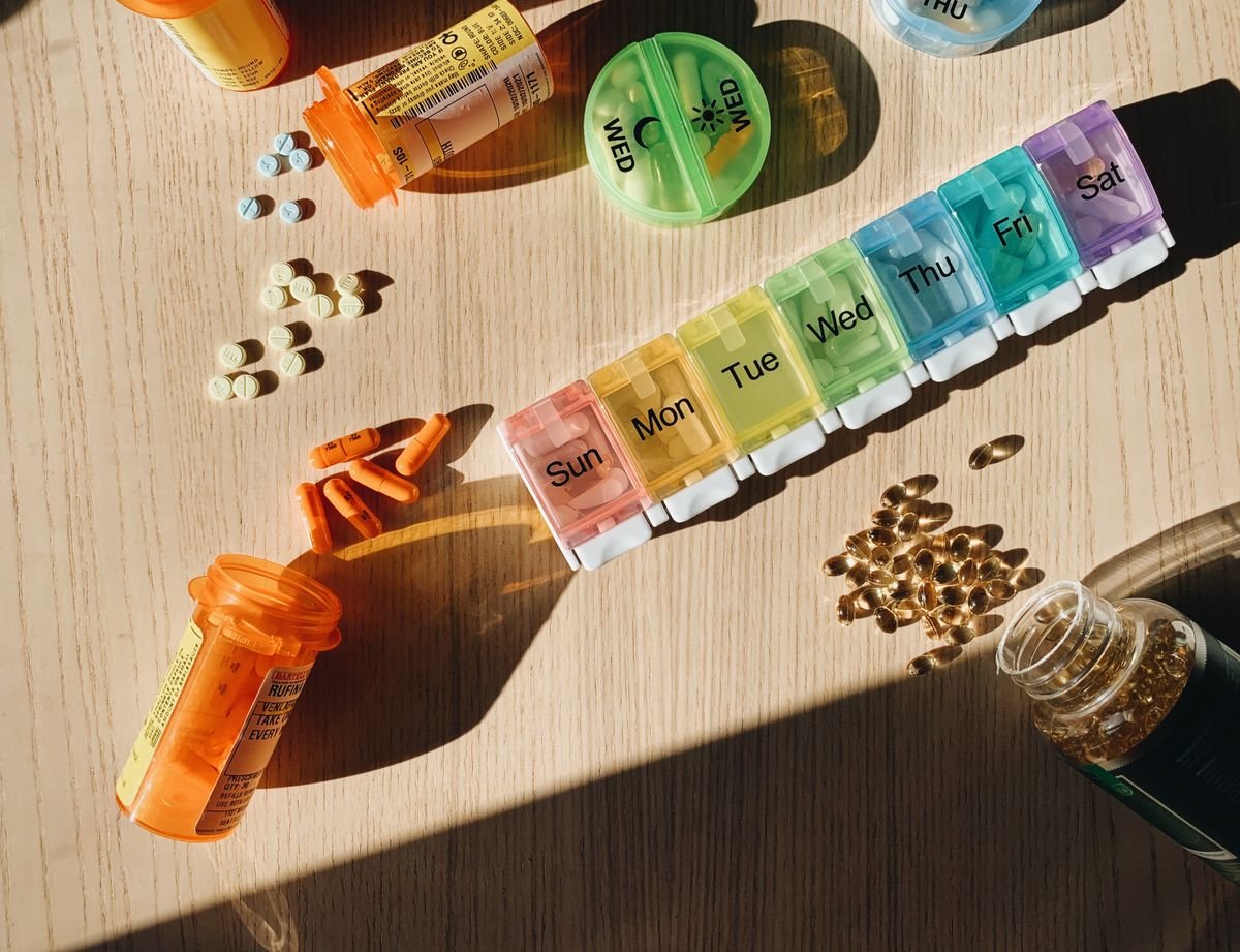 Weekly pill organizer with medication bottles on a wooden table